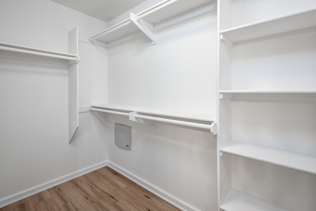 a walk in closet with white shelves and a wood floor