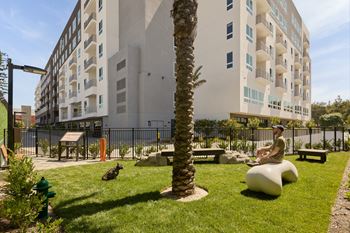 A man is sitting on a white bench in a park with a palm tree and a building in the background.