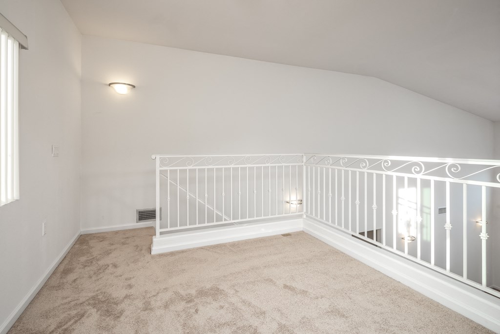 the upstairs loft of a new home with a white railing and carpet