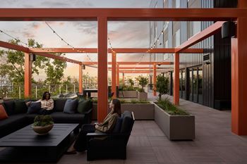 Two women are sitting on a couch under a pergola.