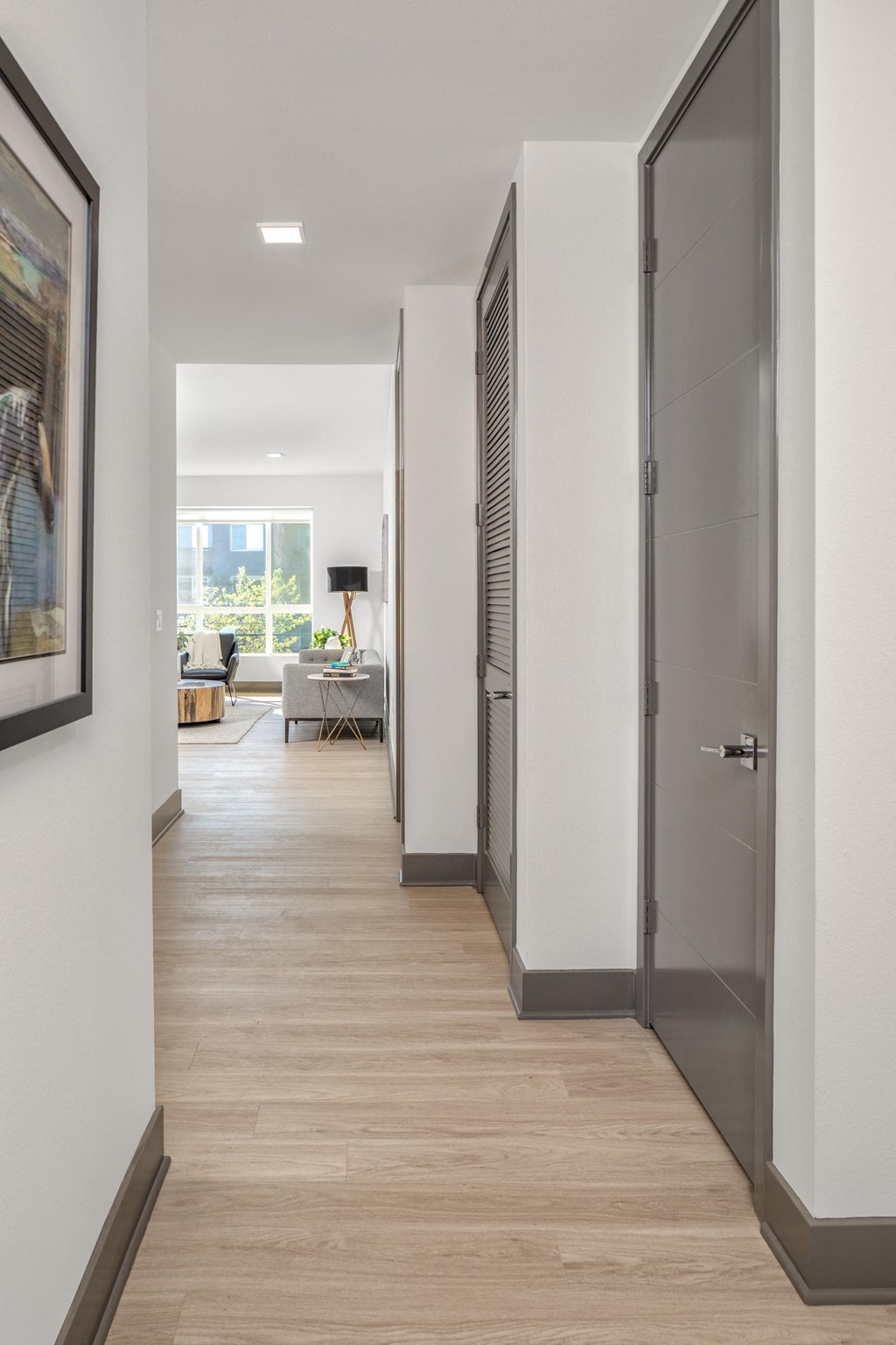 a long hallway with white walls and wood flooring and grey doors