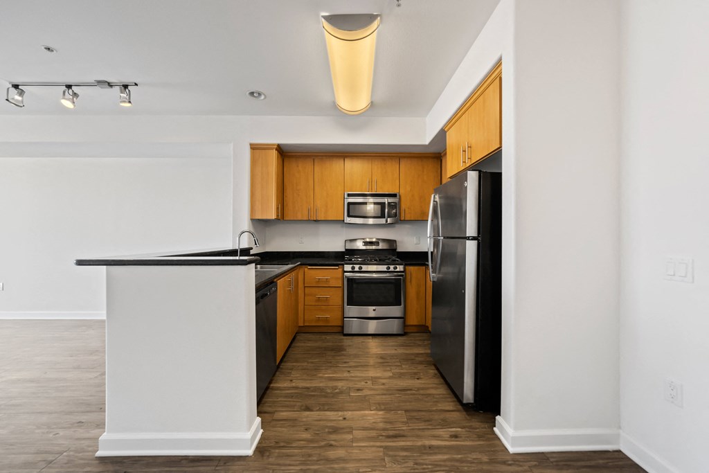 an empty apartment kitchen with black countertops and stainless steel appliances