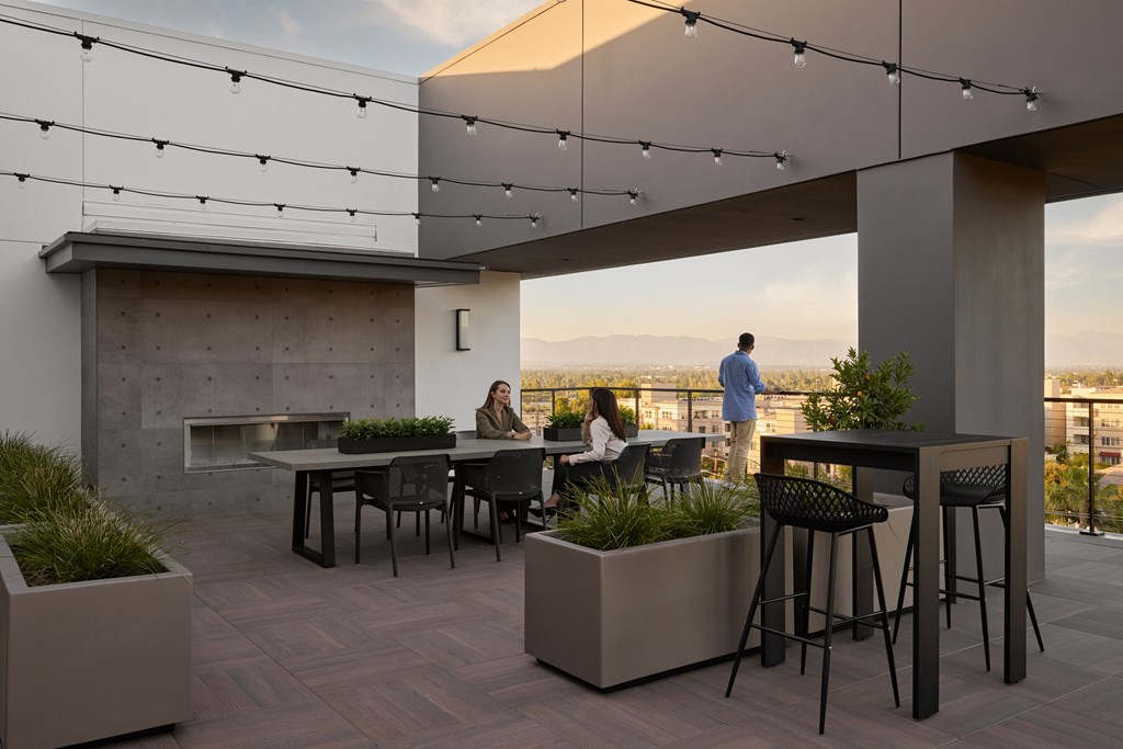 A rooftop patio with people sitting at tables and a view of the city.