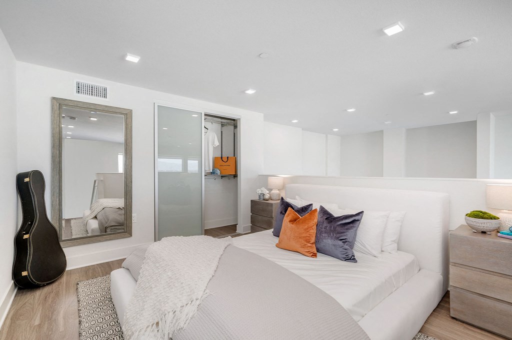 a white bedroom with a large bed and a guitar in the corner