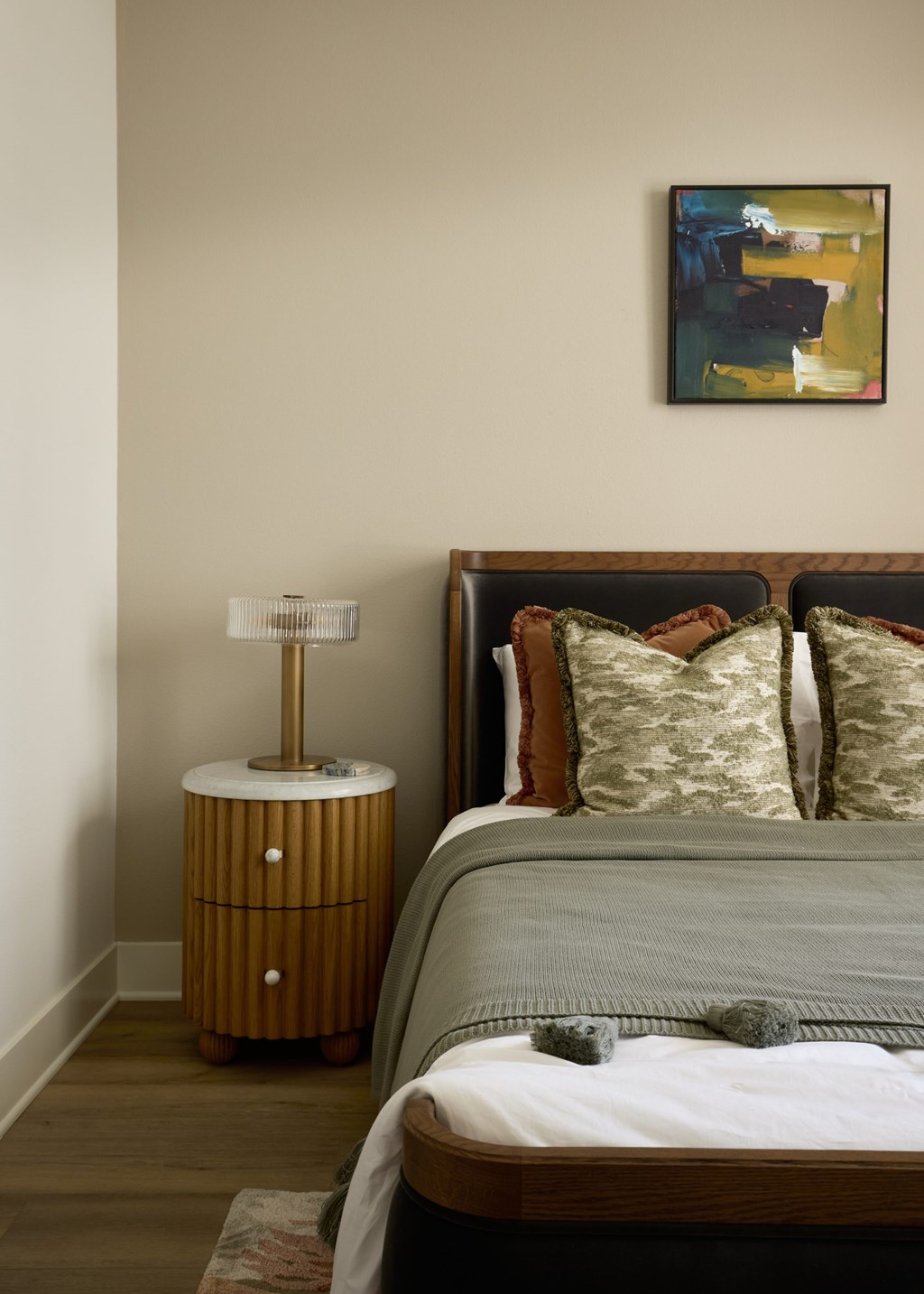 A bedroom with a bed, nightstand, and a painting on the wall.