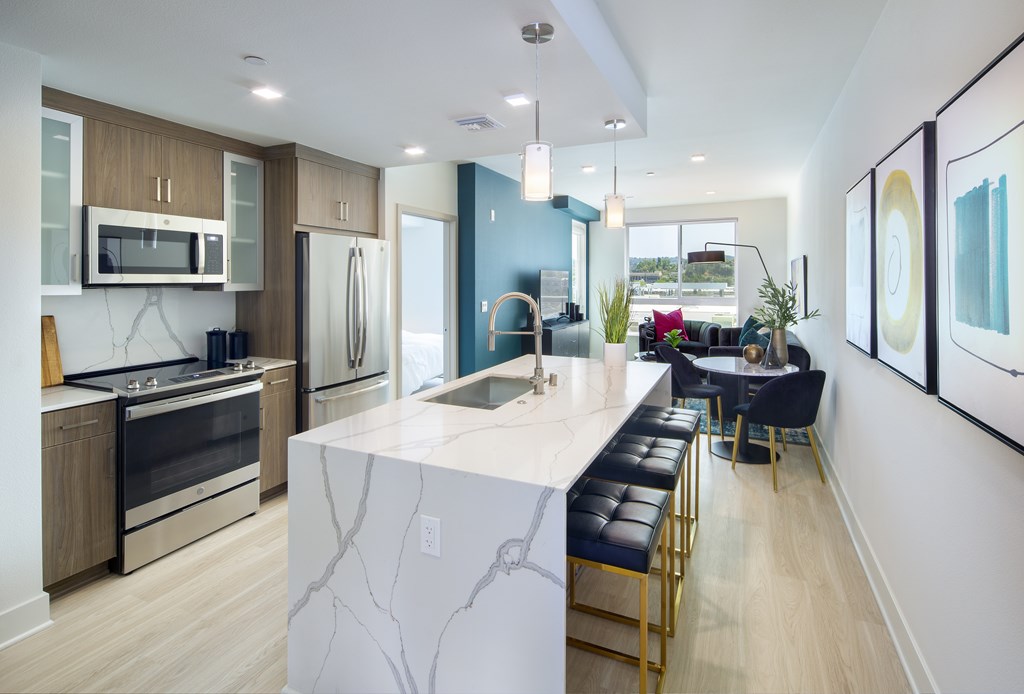 Kitchen Woodland Hills, CA Apartments - The Q Variel - Kitchen with Luxury Vinyl Flooring, Quartz Waterfall Kitchen Island, Advanced Wash Dishwasher, LED Energy-Efficient Lighting Fixtures, and Open-Concept Layout with the Dining Room and Living Room which have High Ceilings and Expansive Windowsirs