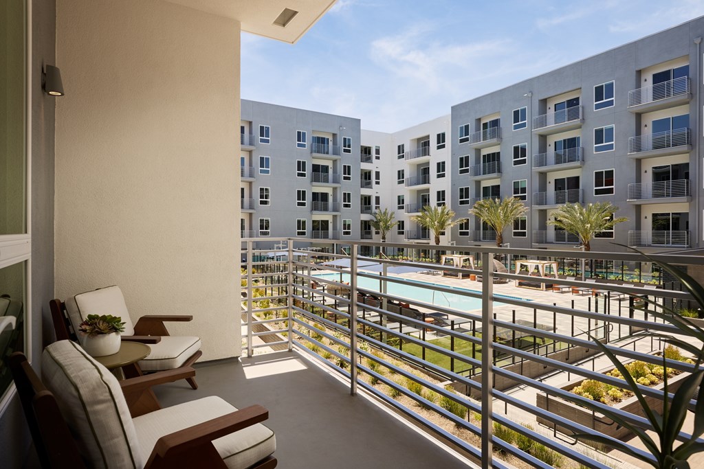 A balcony with chairs and a table overlooks a pool and buildings.
