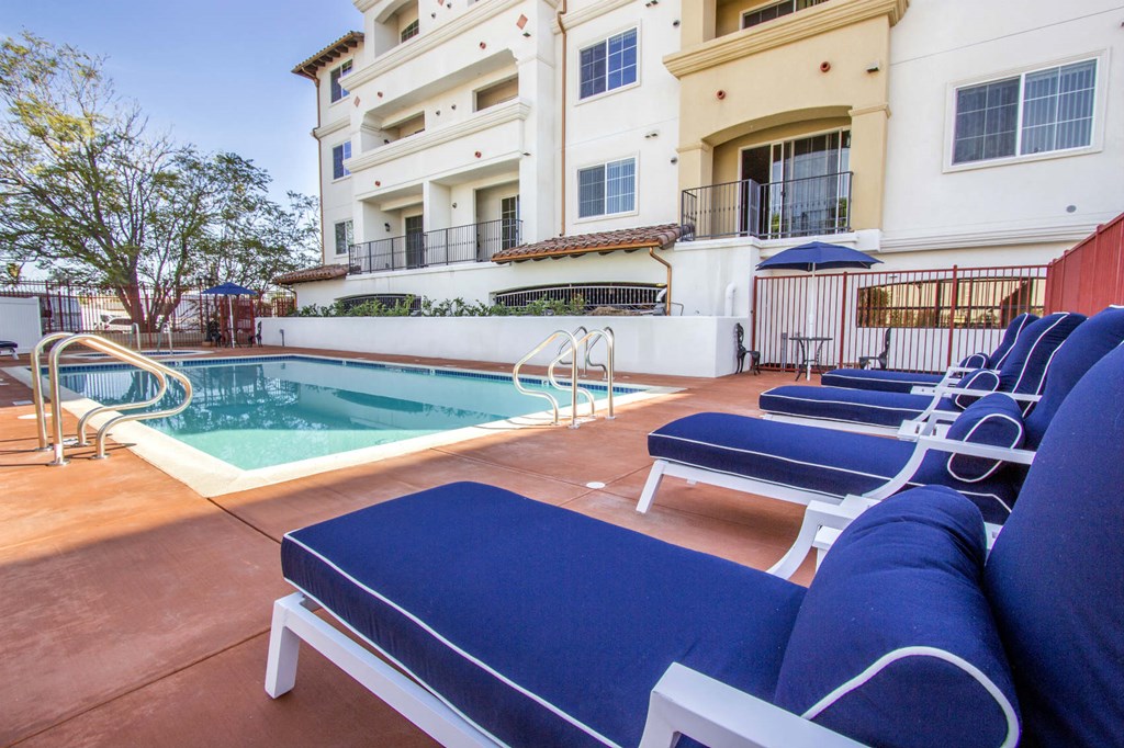 a pool with blue lounge chairs in front of a building