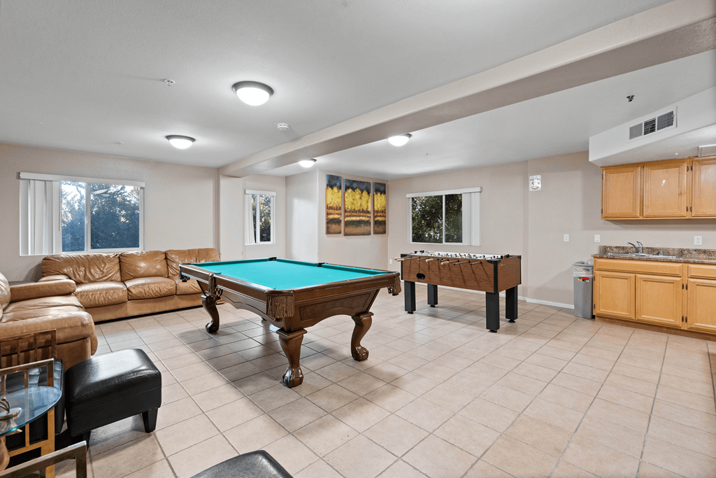 A billiard table is in the middle of a room with a couch and a chair.