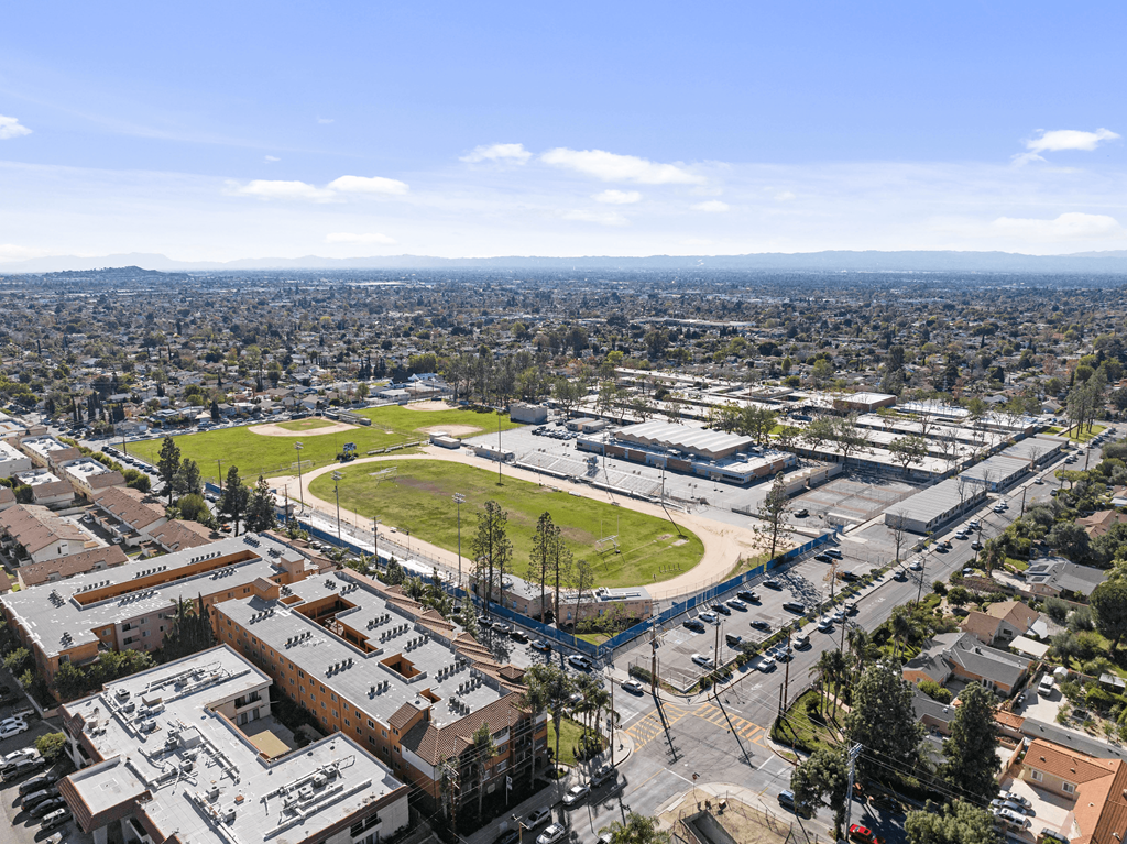 A view of a city from a high vantage point with buildings, a parking lot, and a green field.