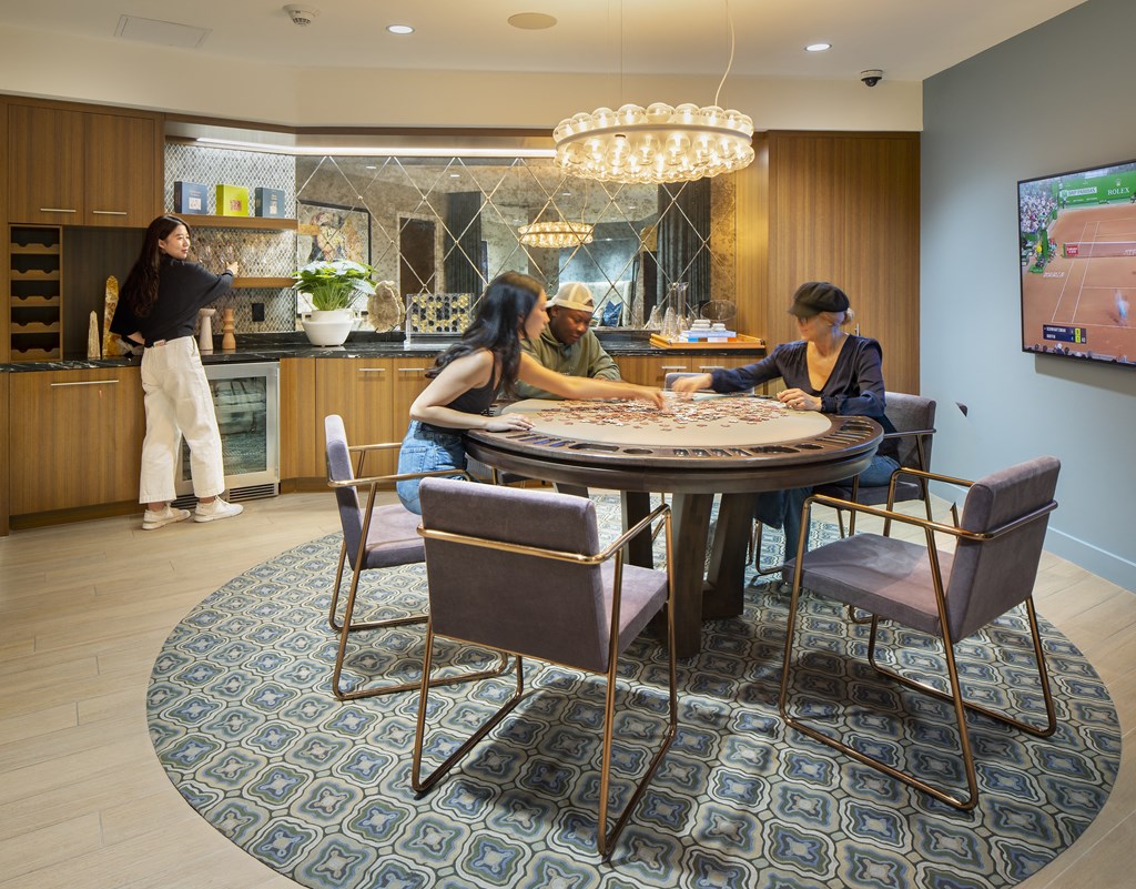 a round table with three people sitting around it and a woman standing in a kitchen in the