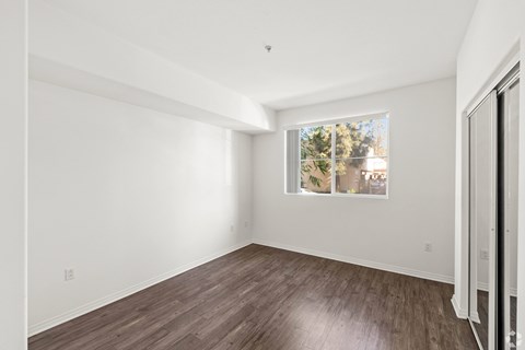 A room with a window showing a view of trees and a wooden floor.
