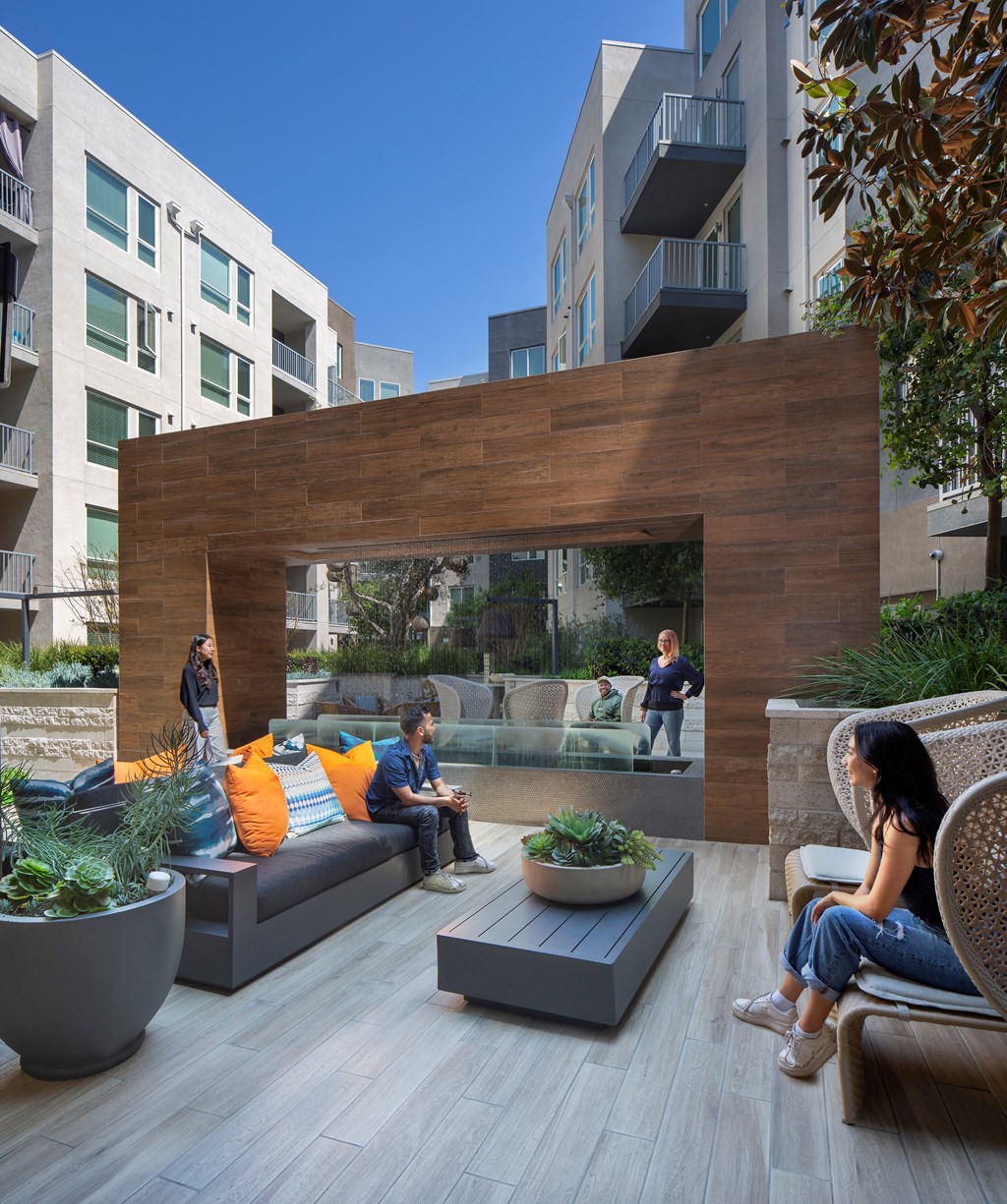 people sitting on couches and chairs on a patio with a wooden wall in the background