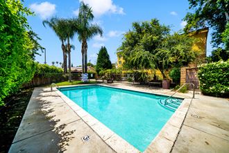 a swimming pool with palm trees and a house in the background at Toscana Apartments, Van Nuys