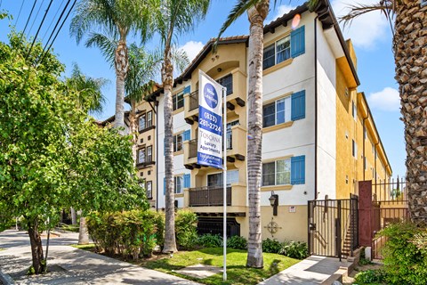 an apartment building with palm trees and a blue and white street sign