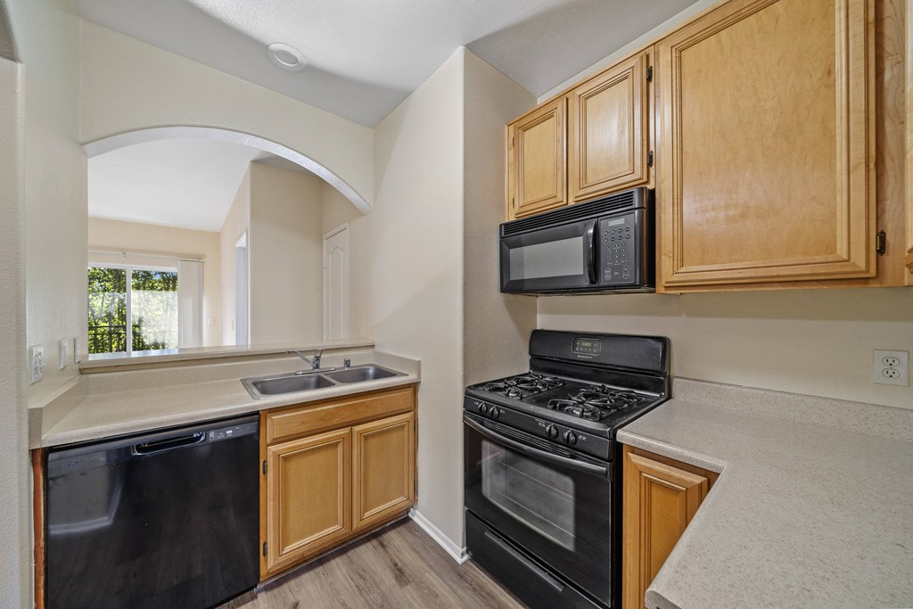 a kitchen with wooden cabinets and black appliances at The Village Apartments, Van Nuys, 91406