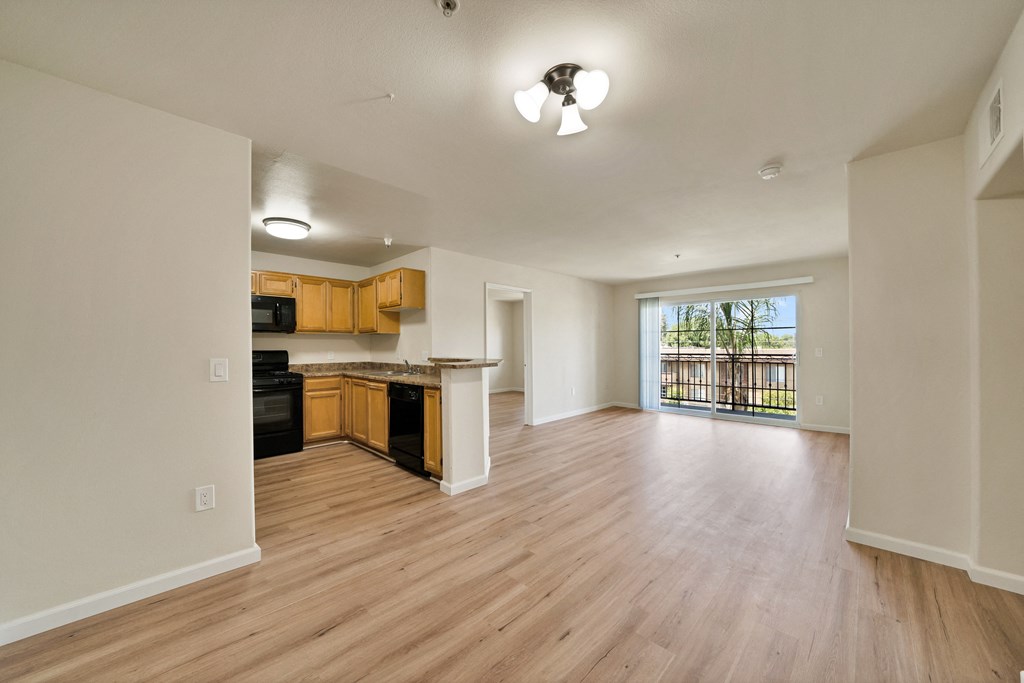 an empty living room and kitchen with wood flooring and a large window