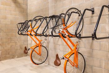 A row of orange bicycles are parked on a bike rack.