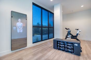 A room with a treadmill, a tablet on the wall and a window.
