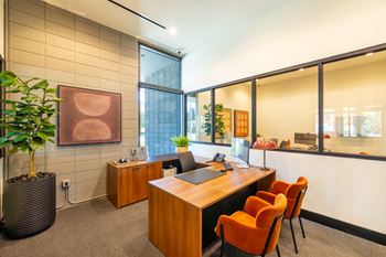 A modern office with a wooden desk and orange chairs.