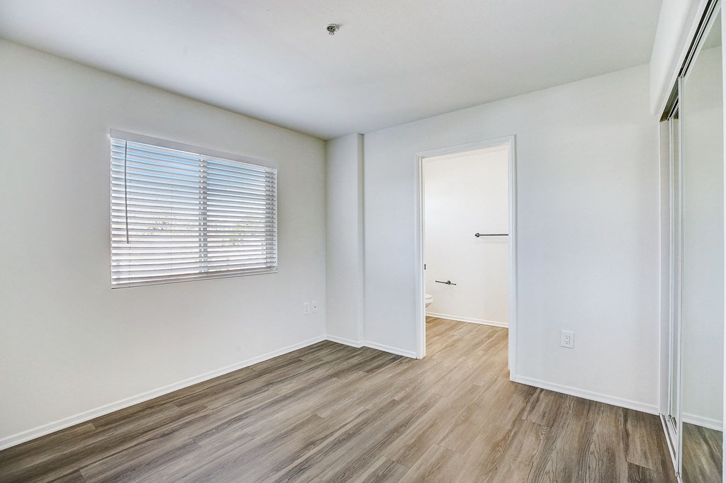 a bedroom with white walls and wood flooring and a door to a closet