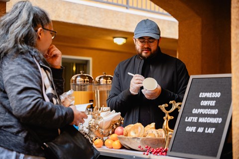 A man in a black outfit is serving coffee to a customer at a cafe.