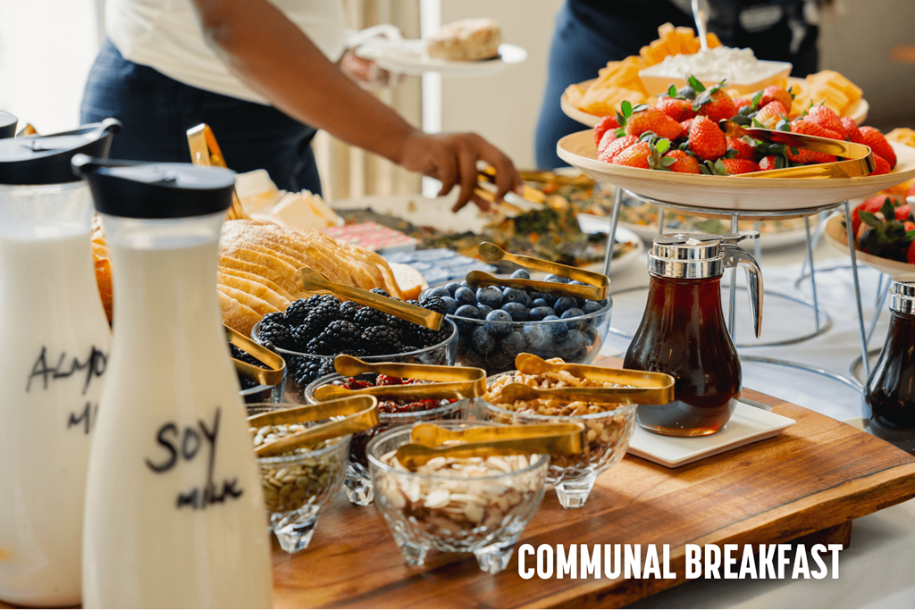A communal breakfast table with various dishes and a sign that says