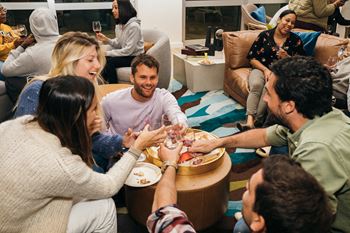 A group of people are gathered around a table, toasting with drinks in their hands.