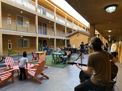 A man is playing guitar in a courtyard with people sitting around a table.