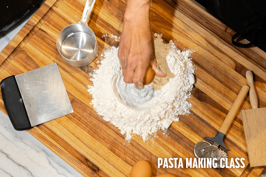 A person is making pasta with a metal scoop and a wooden spatula on a wooden board.