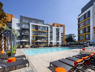 a pool with lounge chairs in front of an apartment building