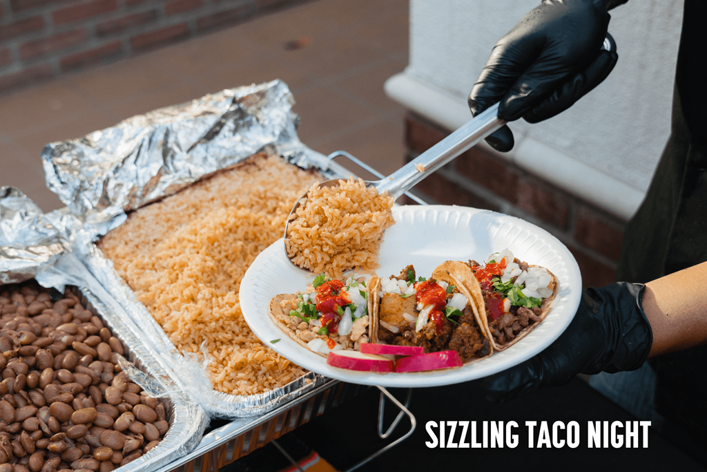A person serving tacos at a Sizzling Taco Night event.