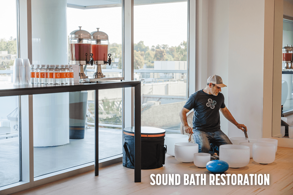 A man is working on a sound bath restoration setup in a room with large windows.