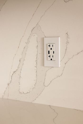 A white electrical outlet on a marble wall.
