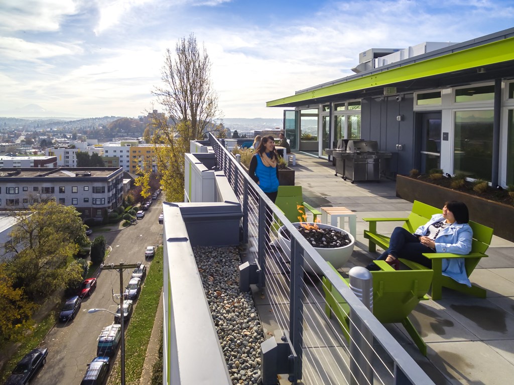 two women sit on green chairs on a roof terrace overlooking a city