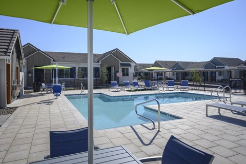 a swimming pool with chairs and umbrellas in front of a house at Village of Chandler Apartments, Chandler, Arizona