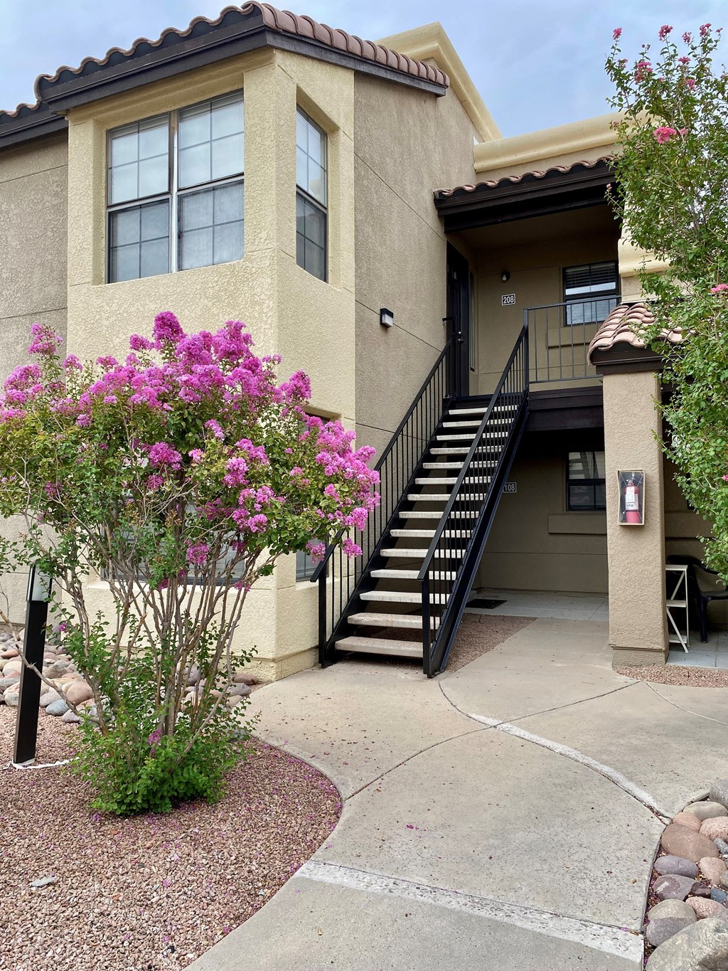 A beige house with a black staircase and pink flowers.