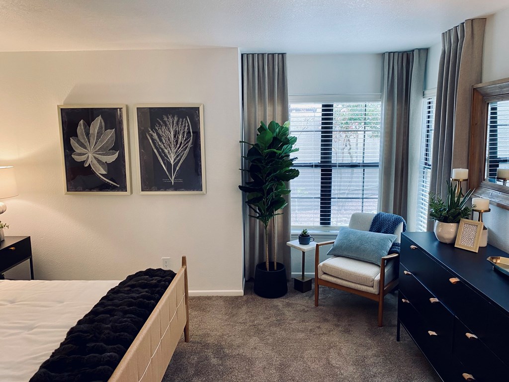 A bedroom with a large bed, a chair, and two framed pictures on the wall.