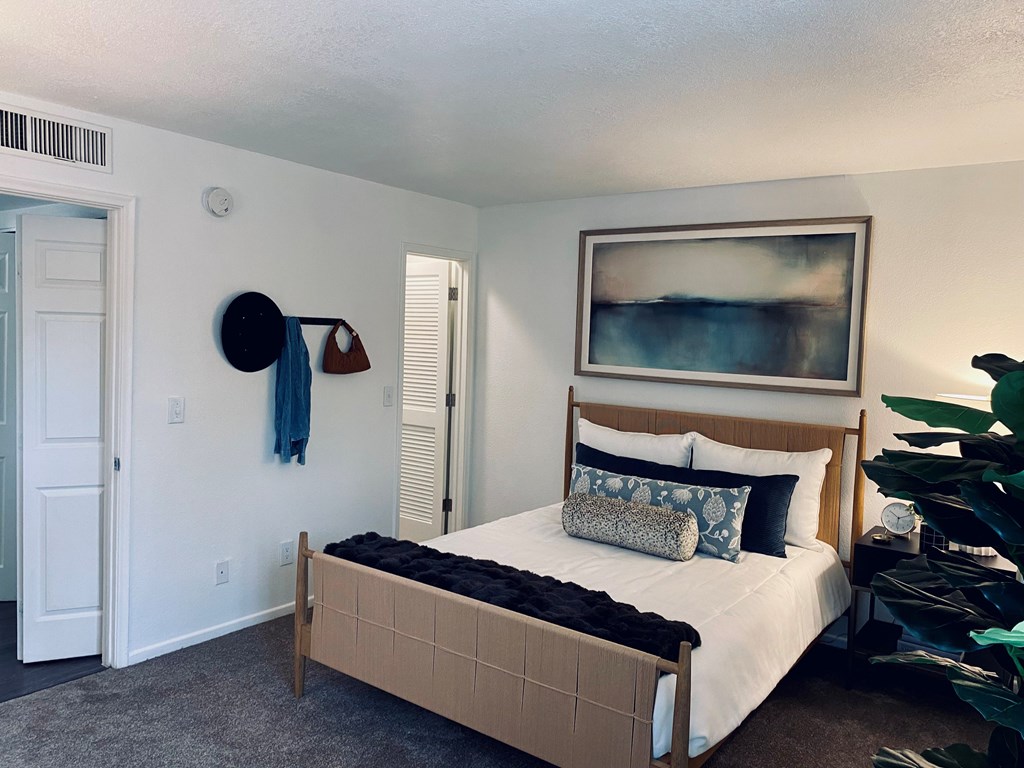 A bedroom with a bed, a painting, a plant, and a door.