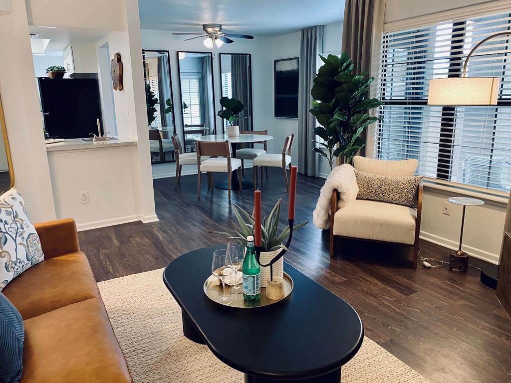 A living room with a brown couch, a black coffee table, and a dining area in the background.
