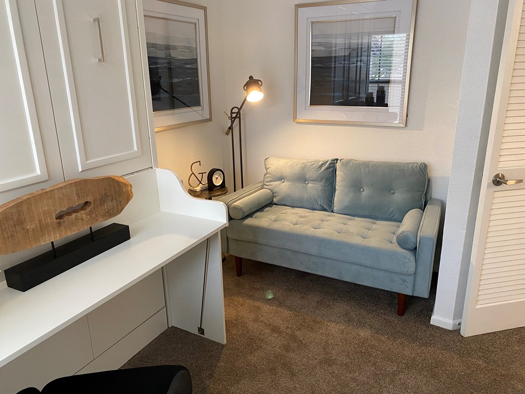A living room with a blue couch and a white desk.