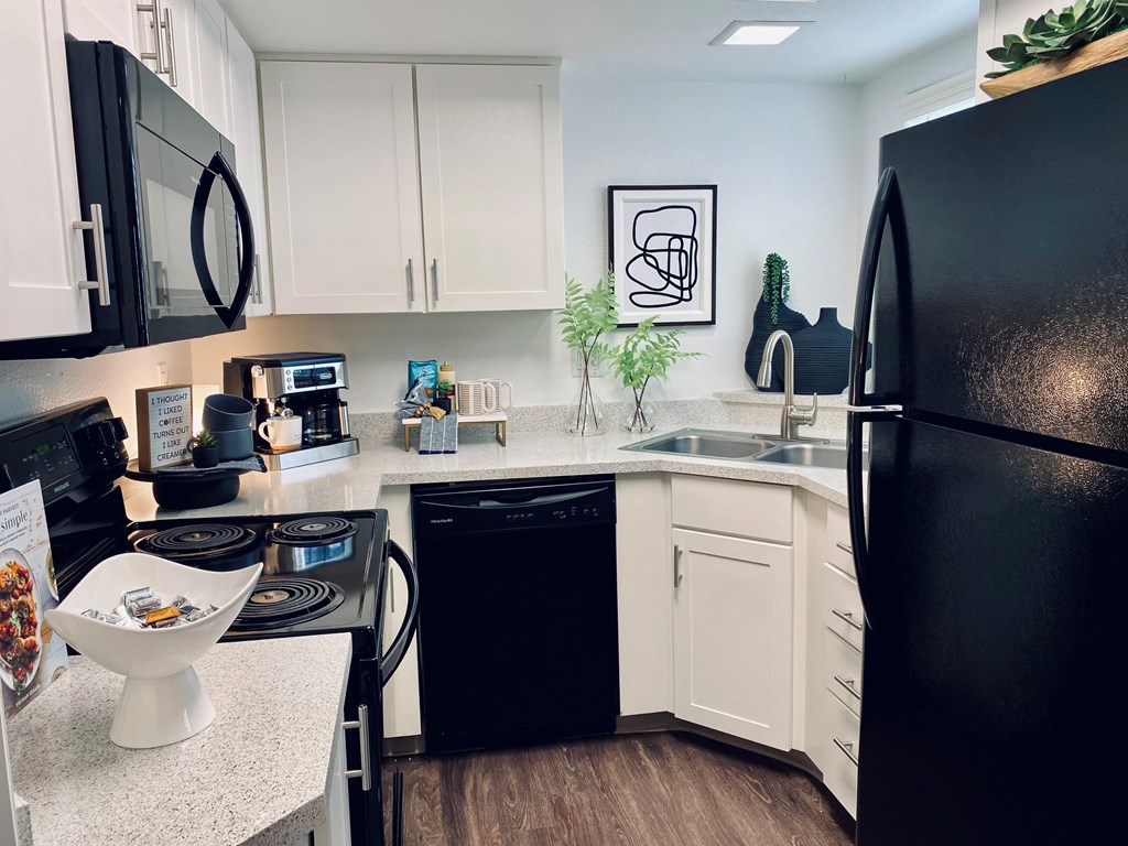 A black refrigerator is on the right in a kitchen with white cabinets.