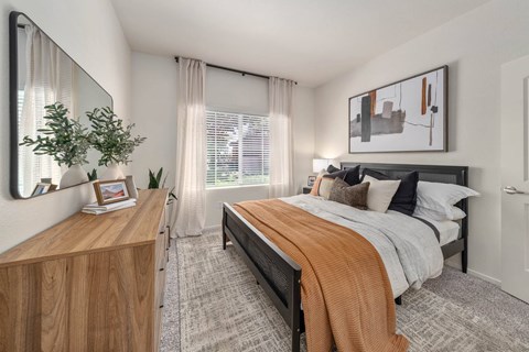 A bedroom with a bed, nightstand, and a mirror on the wall.