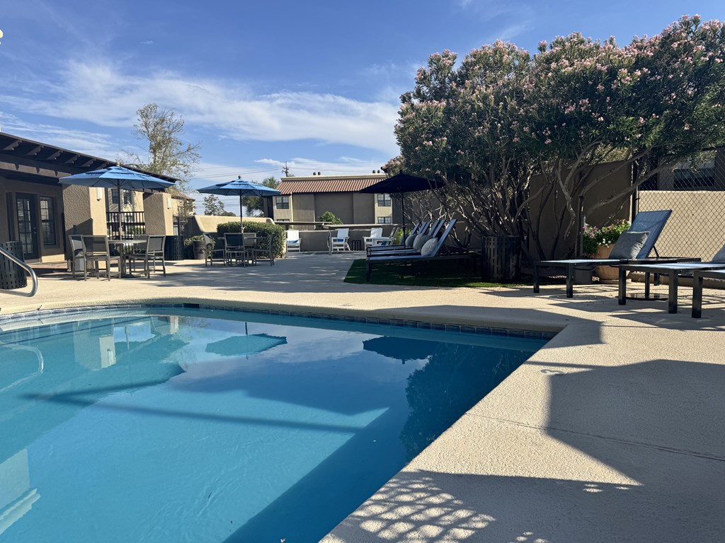 A swimming pool surrounded by a concrete patio and a row of chairs.