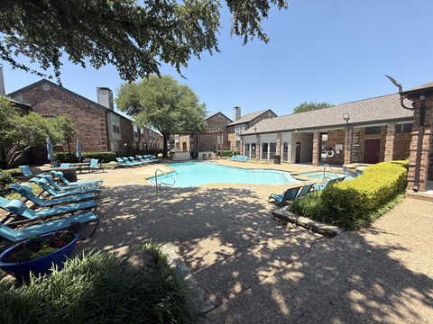 A pool surrounded by a patio with chairs and a hedge.