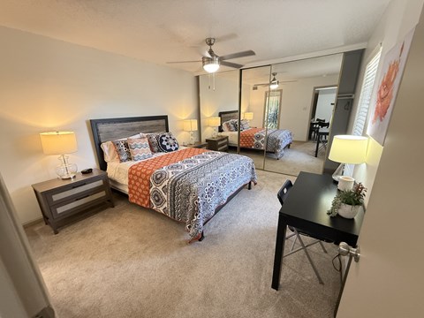 A bedroom with a bed, desk, and mirror.