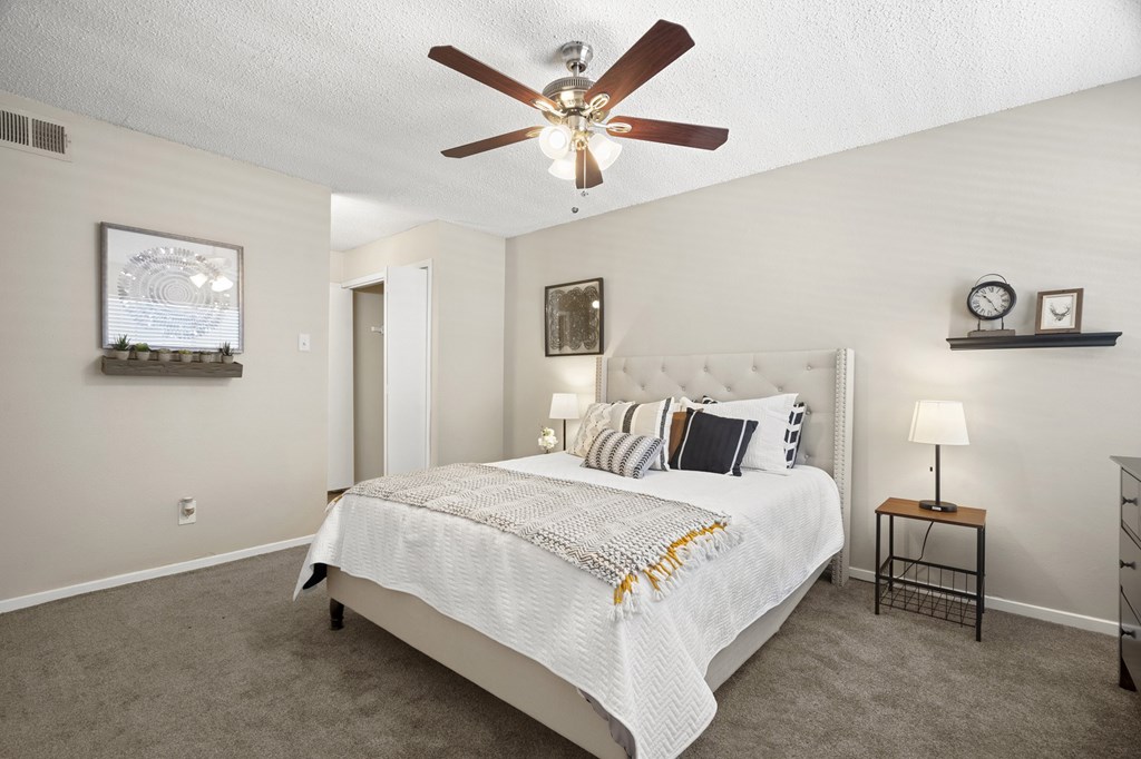 A bedroom with a bed, a ceiling fan, and a nightstand with a lamp.