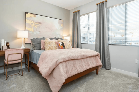 A bedroom with a bed, desk, chair, and a large painting on the wall.