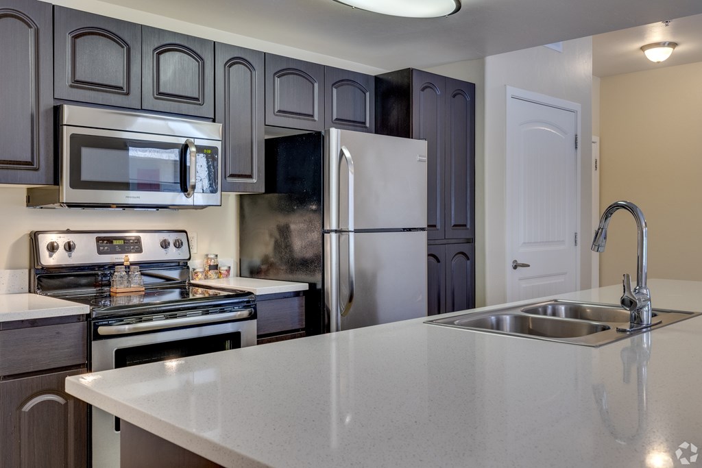 A kitchen with a stove, microwave, refrigerator, and sink.