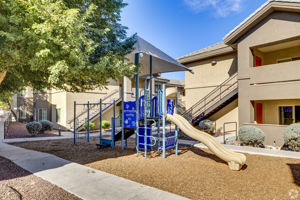 A playground with a blue slide and a yellow slide in front of a building.